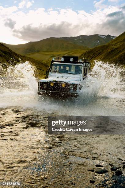 off-road vehicle driving through lake against sky - vehículo de todo terreno fotografías e imágenes de stock
