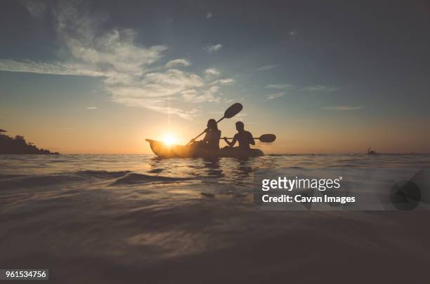 silhouette friends sitting in kayak on sea against sky during sunset - waterfront lifestyle stock pictures, royalty-free photos & images