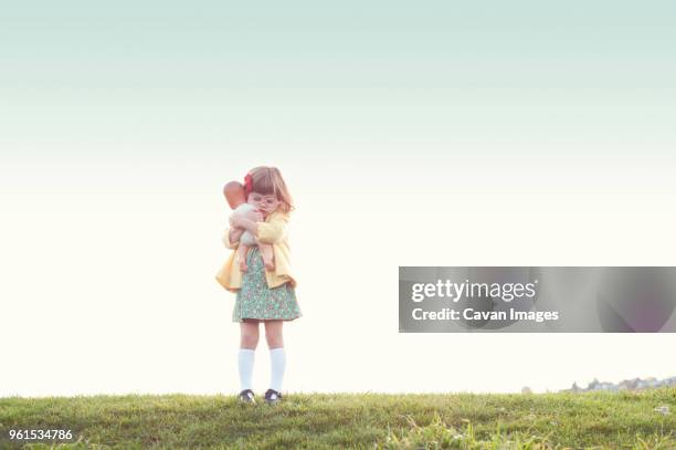 cute girl embracing doll while standing on field against clear sky - doll fotografías e imágenes de stock