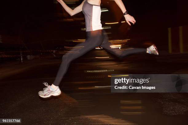 low section of female jogger jumping over puddle in city at night - alleen één jonge vrouw stockfoto's en -beelden