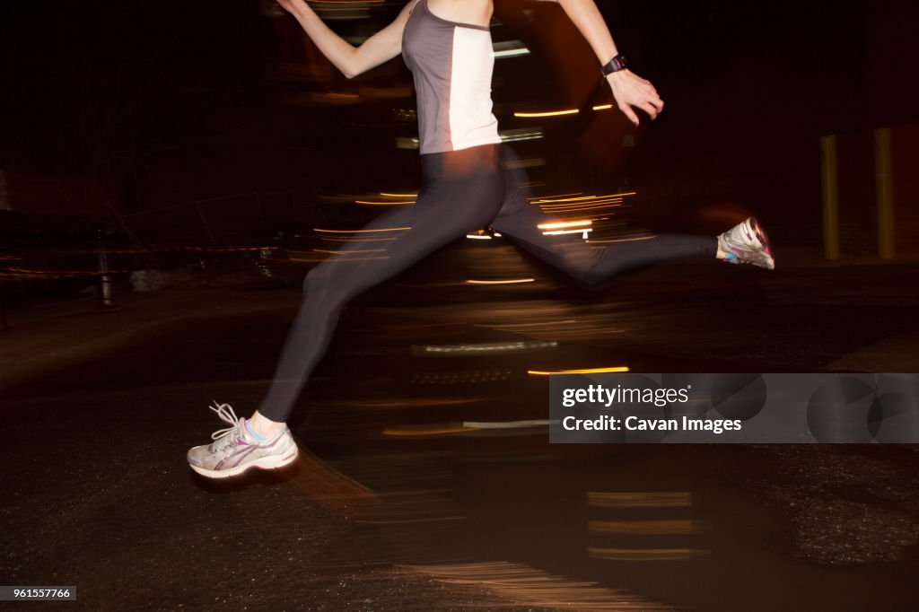 Low section of female jogger jumping over puddle in city at night