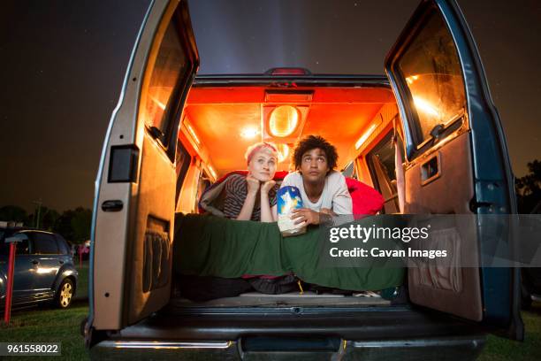couple holding popcorn while sitting in camping van during drive-in movie - girlfriends films stockfoto's en -beelden