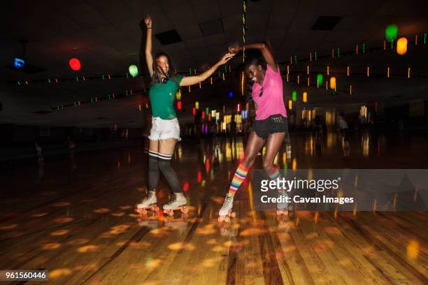 friends dancing while roller skating at illuminated roller rink - roller rink stock-fotos und bilder