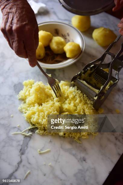 using a fork to remove a pressed boiled potato from a steel potato ricer - potato masher ストックフォトと画像