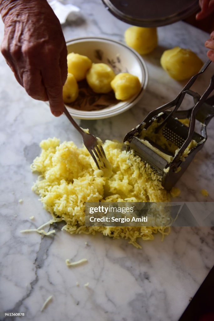 Using a fork to remove a pressed boiled potato from a steel potato ricer