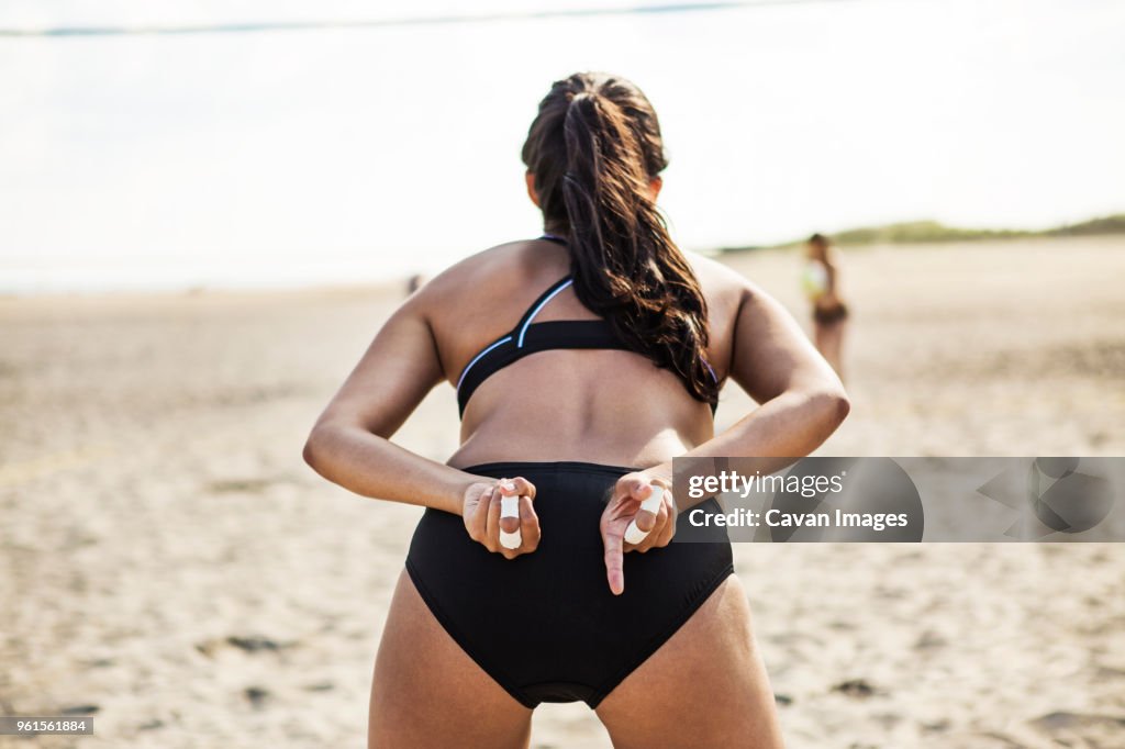 Rear view of woman standing at beach while playing volleyball