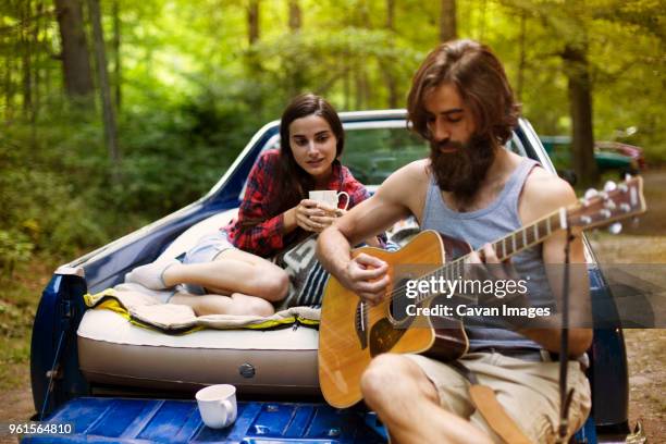 man playing guitar for girlfriend while sitting in pick-up truck at forest - guitar pick stock pictures, royalty-free photos & images