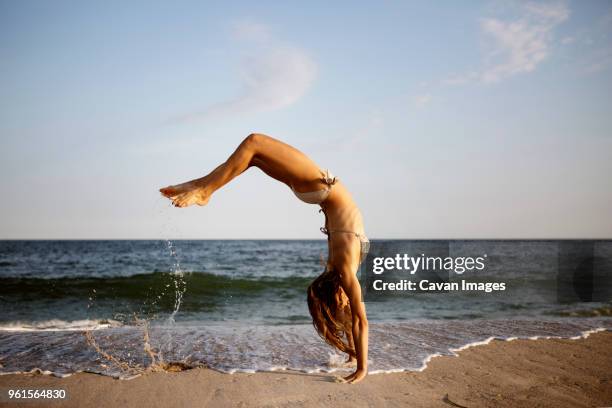 side view of woman doing back flip at beach against sky - fare le capriole all'indietro foto e immagini stock