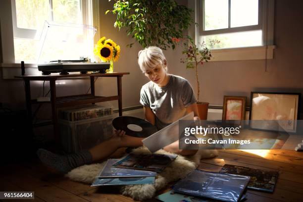 young woman looking at vinyl records while sitting on floor at home - vinylplaat stockfoto's en -beelden