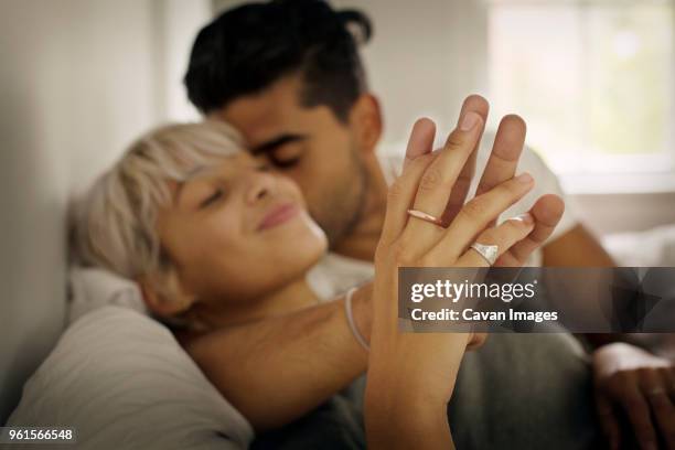 affectionate young man kissing woman while holding hand in bedroom - anillo joya fotografías e imágenes de stock