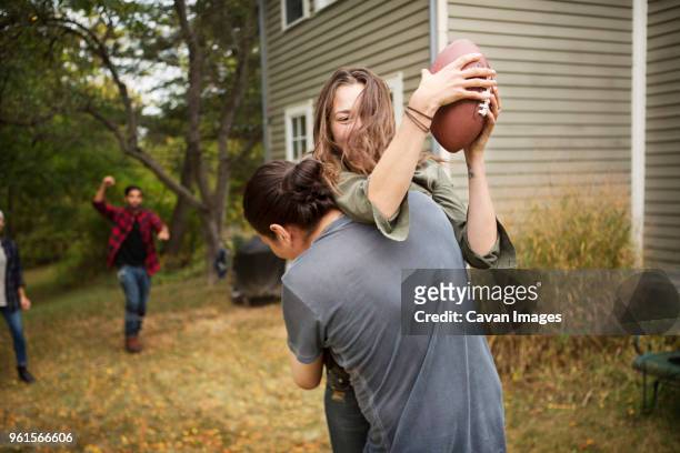 couple playing football with friends on field - tackle american football player stockfoto's en -beelden