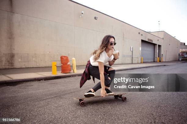 woman drinking smoothie while skateboarding on street - all that skate 2014 stock pictures, royalty-free photos & images