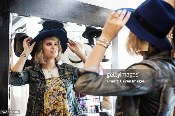 woman trying on hat while standing in front of mirror - chaqueta de ante fotografías e imágenes de stock