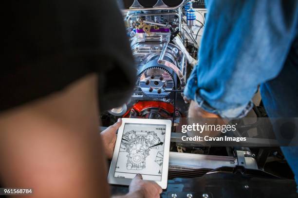 mechanics examining blueprint on tablet computer while repairing engine - auto tablet stock-fotos und bilder