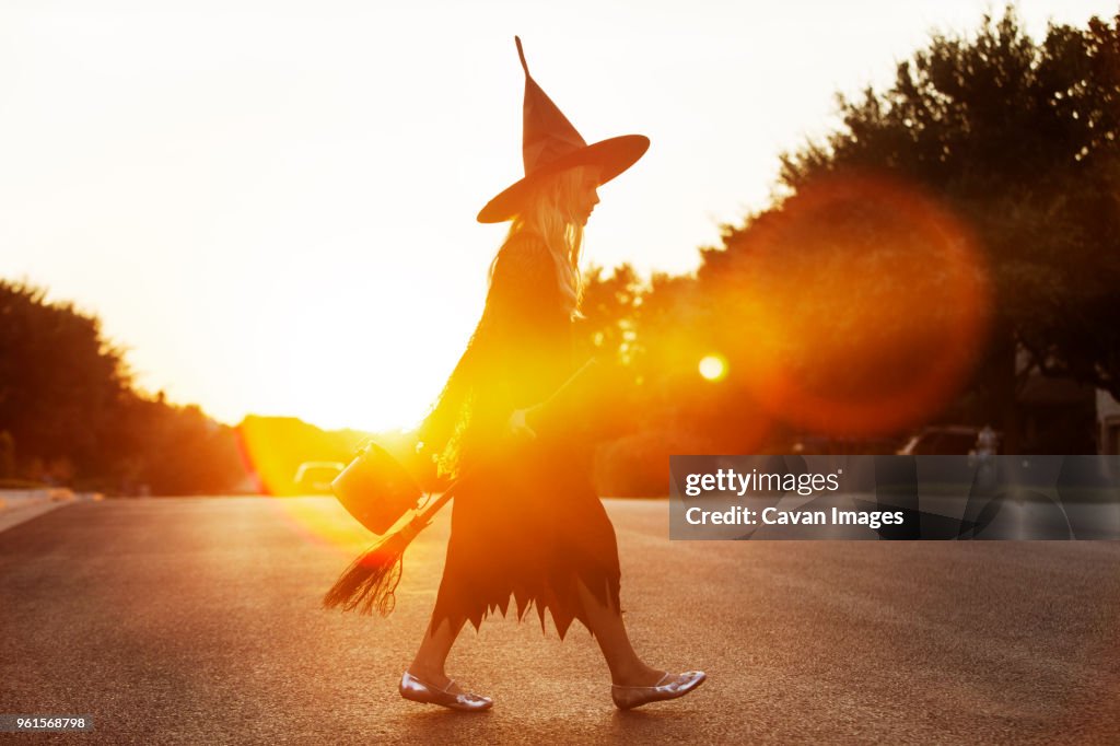 Girl dressed in witch costume walking on road during sunset