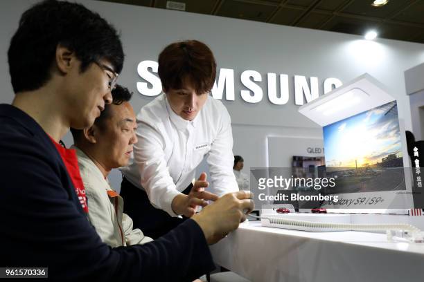 Booth attendant, right, demonstrates using a Samsung Electronics Co. Galaxy S9 smartphone to visitors at the World IT Show 2018 in Seoul, South...