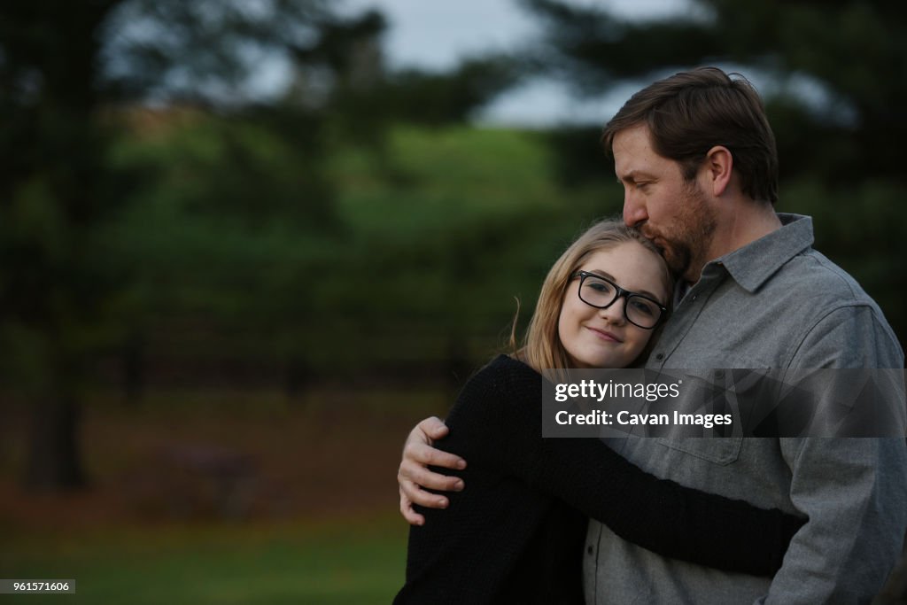 Father kissing daughter while standing at yard