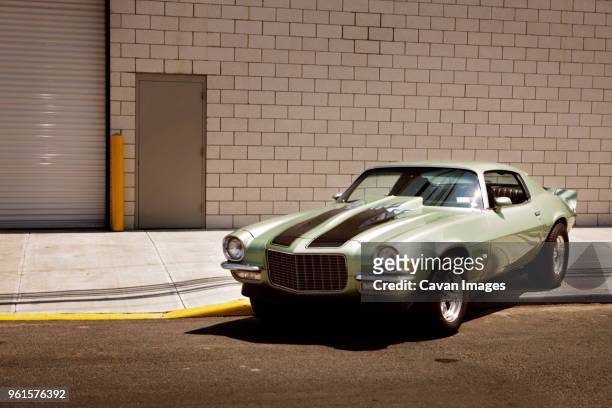 green car on footpath against building in city - vintage car stock pictures, royalty-free photos & images