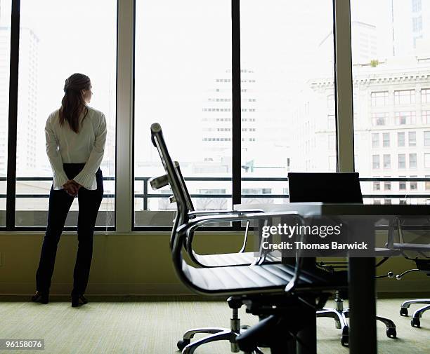 businesswoman standing looking out office window - regisseurstoel stockfoto's en -beelden