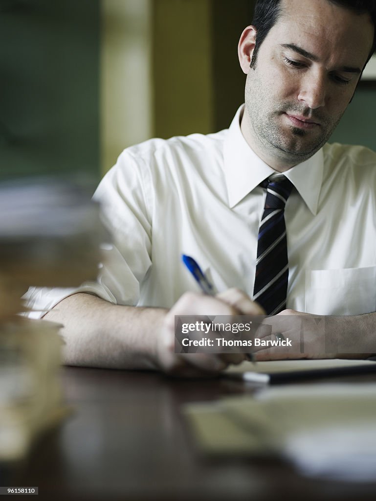 Businessman writing at cluttered desk in office