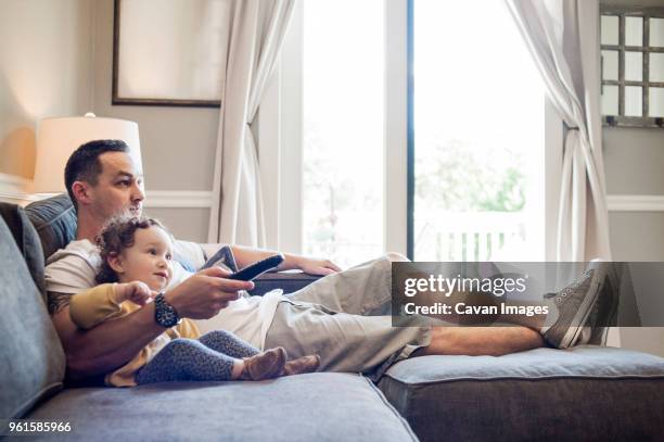 father and daughter watching television at home - genderblend2015 stock pictures, royalty-free photos & images