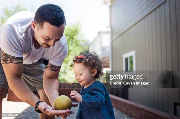 father giving ball to baby while standing in backyard - genderblend2015 stock pictures, royalty-free photos & images