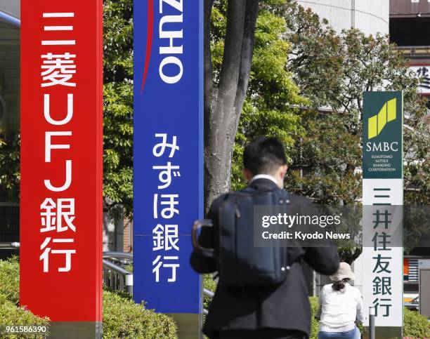 People pass signs for MUFG Bank, Mizuho Bank and Sumitomo Mitsui Banking Corp. In Tokyo's Koto Ward on May 11, 2018. ==Kyodo