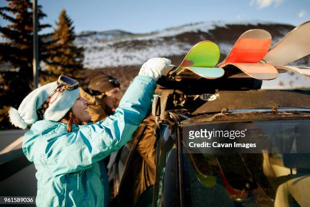 side view of woman removing skis from car while standing by friend at ski resort - vacanza sulla neve foto e immagini stock