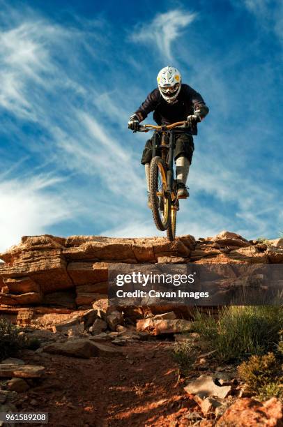 mountain biker jumping from cliff against sky - mann freudensprung sonne vorderansicht leger stock-fotos und bilder