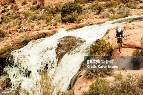 high angle view of male cyclist riding bicycle by waterfall - confidence male landscape stock-fotos und bilder