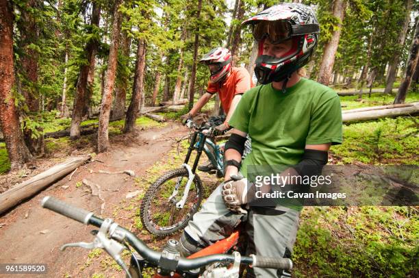 mountain bikers looking away while sitting on bicycles in forest - gloves clasped hands ストックフォトと画像