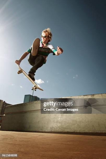 low angle view of man jumping with skateboard against sky - mann freudensprung sonne vorderansicht leger stock-fotos und bilder