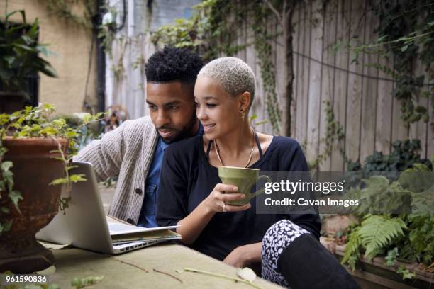 woman holding coffee cup sitting with boyfriend using laptop computer in backyard - using laptop outside stock pictures, royalty-free photos & images