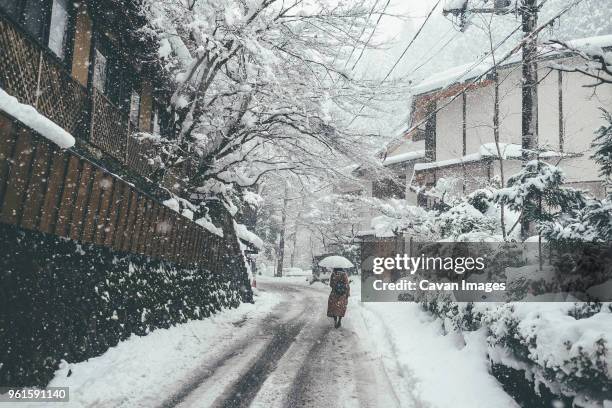 rear view of woman holding umbrella while walking on snow covered road during snowfall in city - kyoto covered with first snow of the season stock-fotos und bilder