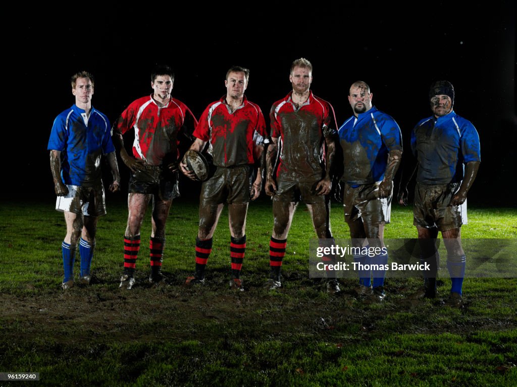 Six male rugby players covered in mud on field