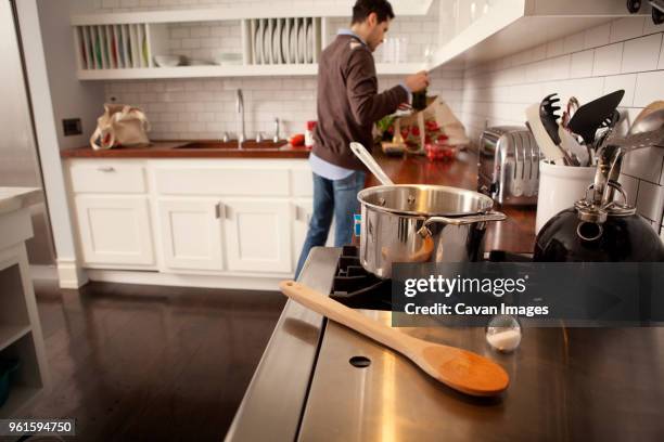 man removing groceries from shopping bag in kitchen - saucepan - fotografias e filmes do acervo