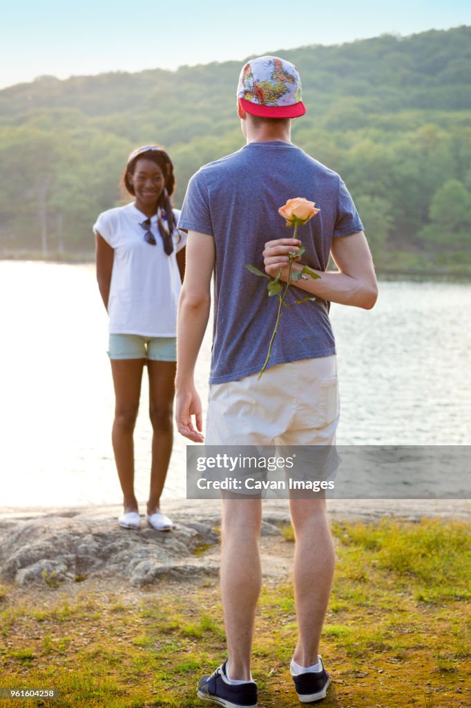Rear view of man hiding rose behind back to propose girlfriend