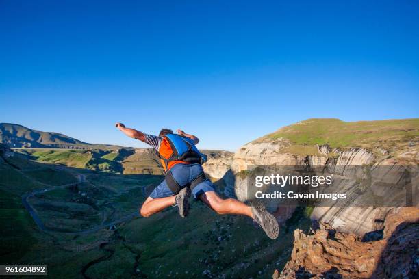 rear view of man base jumping from mountain - base jumping stock pictures, royalty-free photos & images