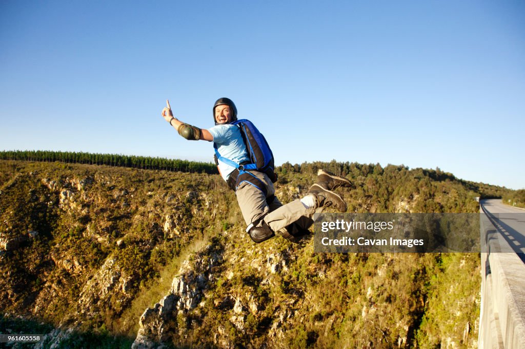 Side view of man base jumping against clear sky