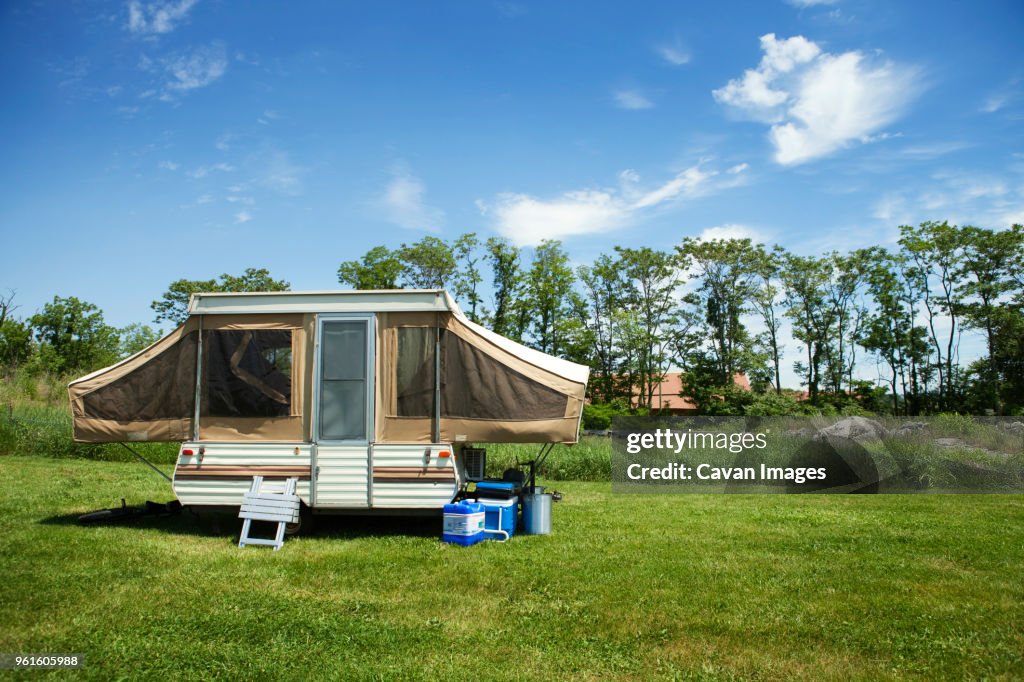 Trailer home on grassy field against cloudy sky