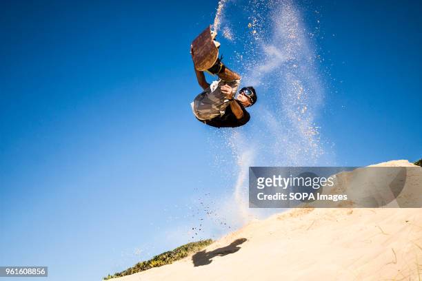 Sandboarder doing a front flip against cloudless blue sky and holding his board on sand dunes. Sandboarding is an activity similar to snowboarding...