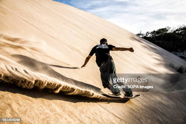 Sandboarder sliding on a dune. Sandboarding is an activity similar to snowboarding but takes place on sand dunes rather than snow-covered mountains....