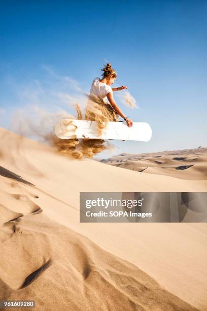 Female sandboarder jumping on a dune in Peruvian desert. Sandboarding is an activity similar to snowboarding but takes place on sand dunes rather...