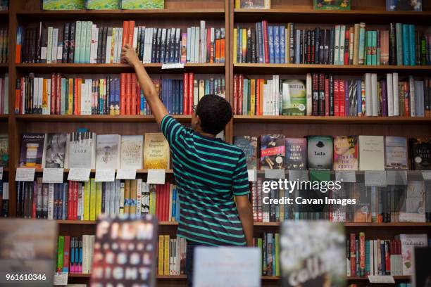 rear view of man removing book from shelf while standing in store - shelf strip stock pictures, royalty-free photos & images