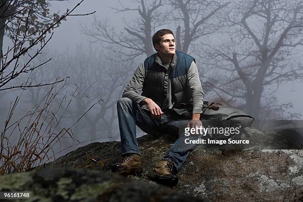 a male hiker sitting on a rock in a misty forest - outdoor guy sitting on a rock stockfoto's en -beelden