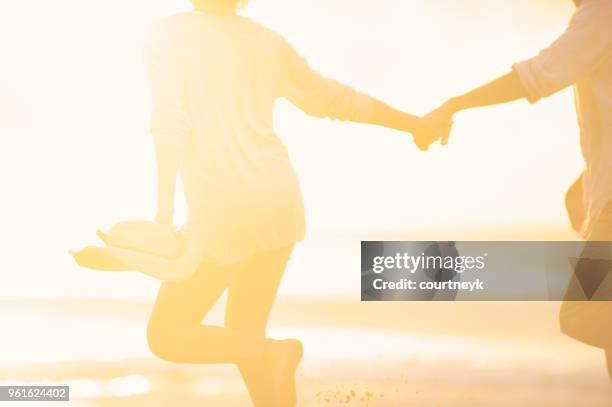 paar entlang des strandes händchenhalten bei sonnenaufgang oder sonnenuntergang. - blurred running sunset stock-fotos und bilder