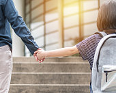 Girl kid (elementary student) carrying backpacks holding parent mother's hand walking up educational building's stair going to class for back to school first day and bring kid to work concept