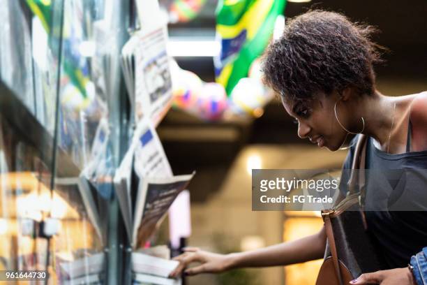 afro young woman looking for the news at newsstand - banca de jornais imagens e fotografias de stock