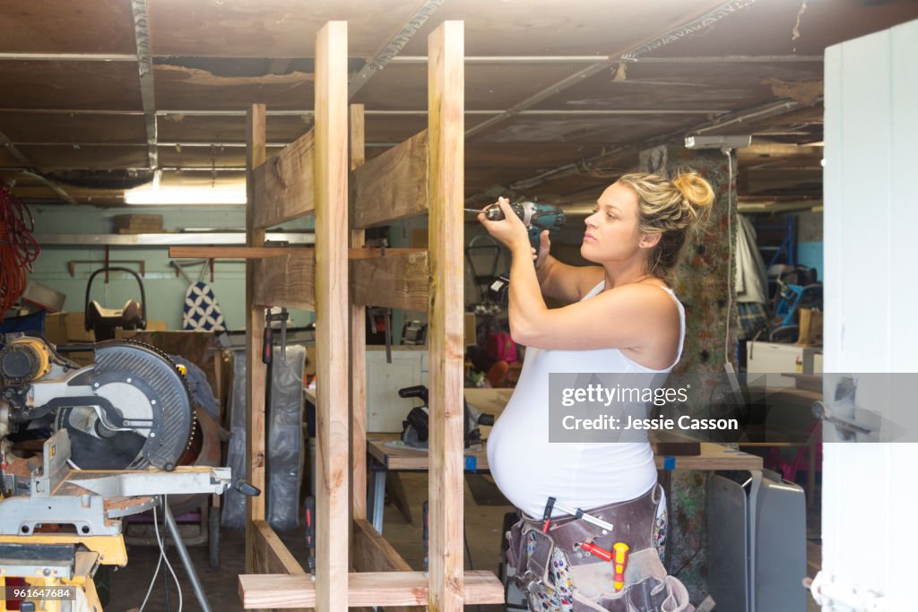 A pregnant woman does DIY with a drill in a messy workshop