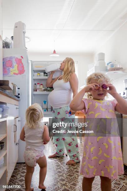 pregnant woman drinks milk from the fridge in a retro kitchen with her two children - funny fridge stock pictures, royalty-free photos & images